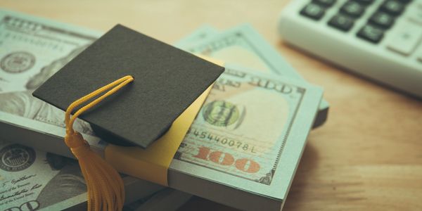 stacks of bills with a graduate cap sitting on top. 
