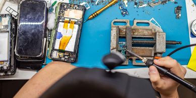 Hands repairing a smartphone on a cluttered workbench.