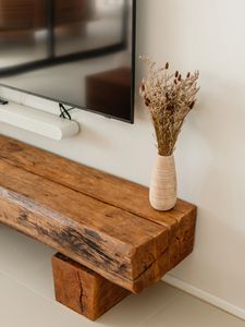 Rustic wooden bench with vase and TV above.