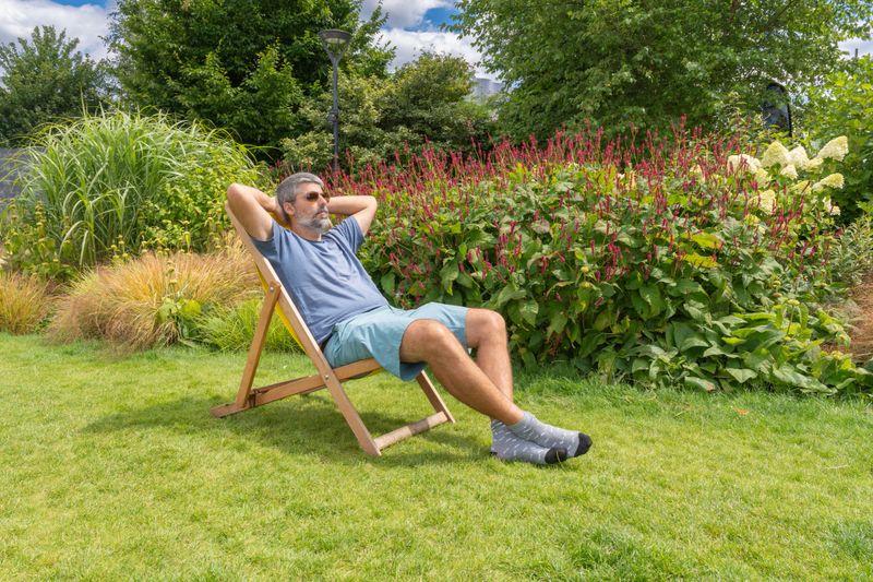 Mid adult man relaxing in a deck chair on a sunny summer day, enjoying the tranquility of his garden filled with greenery and flowers