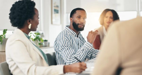 A man in a striped shirt speaks during a business meeting with colleagues.