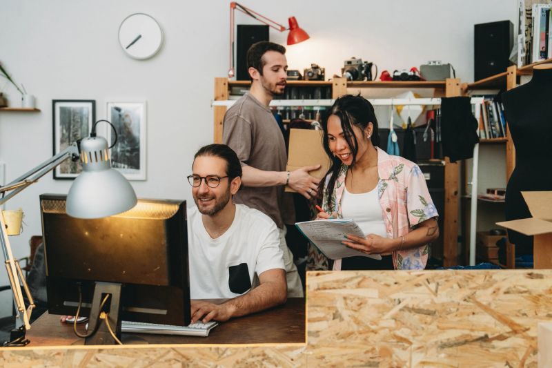 Young entrepreneurs collaborating on a project, using computer and taking notes, in a modern co-working space