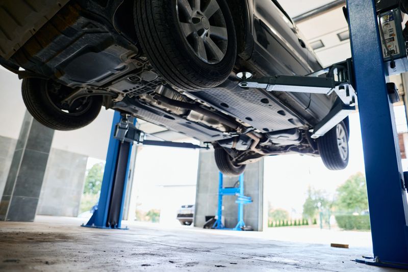 Modern car elevated on a hydraulic lift inside a clean, organized repair shop, with a mechanic inspecting and fixing the vehicle for optimal performance and safety