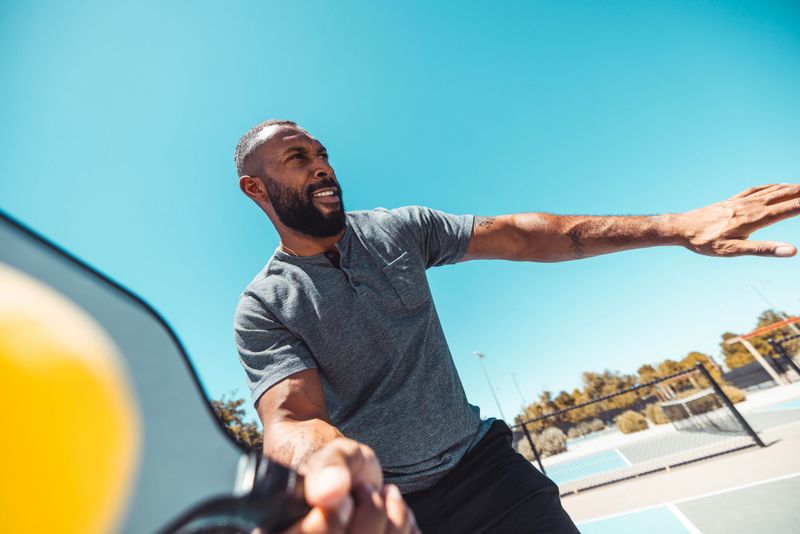 An African American man playing pickleball at the park.