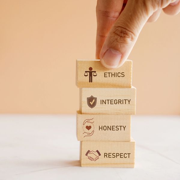 Fingers stacking small wooden blocks, individually labelled: ethics, integrity, honesty, respect.
