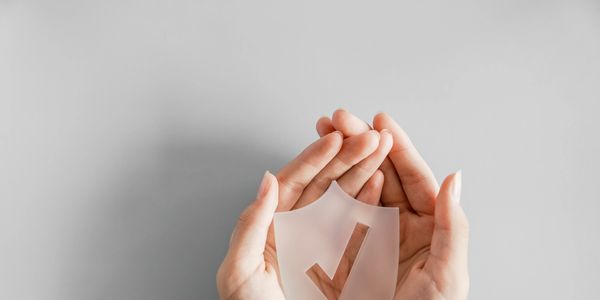 Hands gently holding a shield with a checkmark symbolizing protection and security.