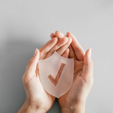 Hands holding a shield with a checkmark symbol.