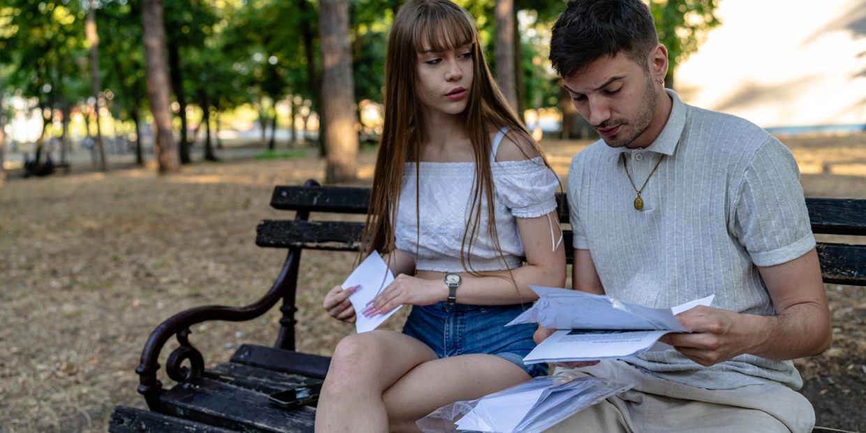 A young couple reviewing papers together on a park bench.