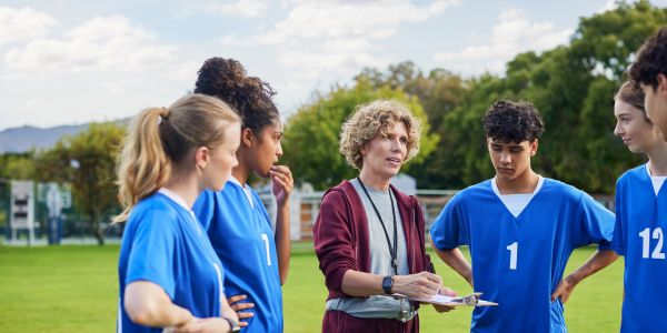 Coach discussing strategy with soccer players on field.