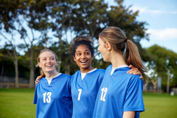 Tres chicas en camisetas azules sonríen en un campo.