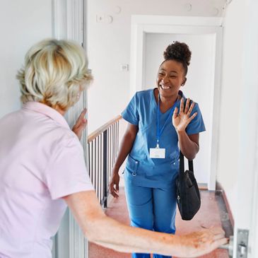 Healthcare worker warmly greeting an elderly woman at home.