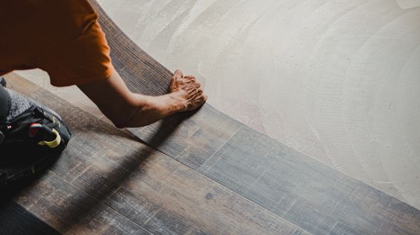 Person installing wood flooring over a concrete base.