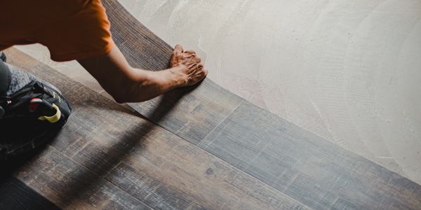 Person installing wood flooring over a concrete base.