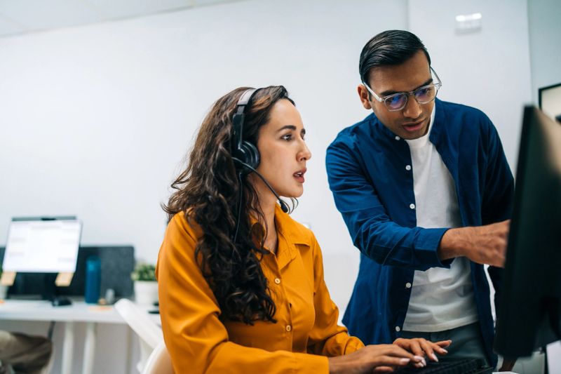 Hispanic Woman in headset receiving guidance from colleague