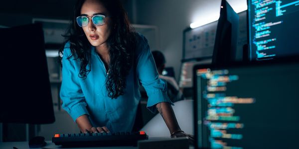 Woman focused on coding at her computer in a dimly lit office.