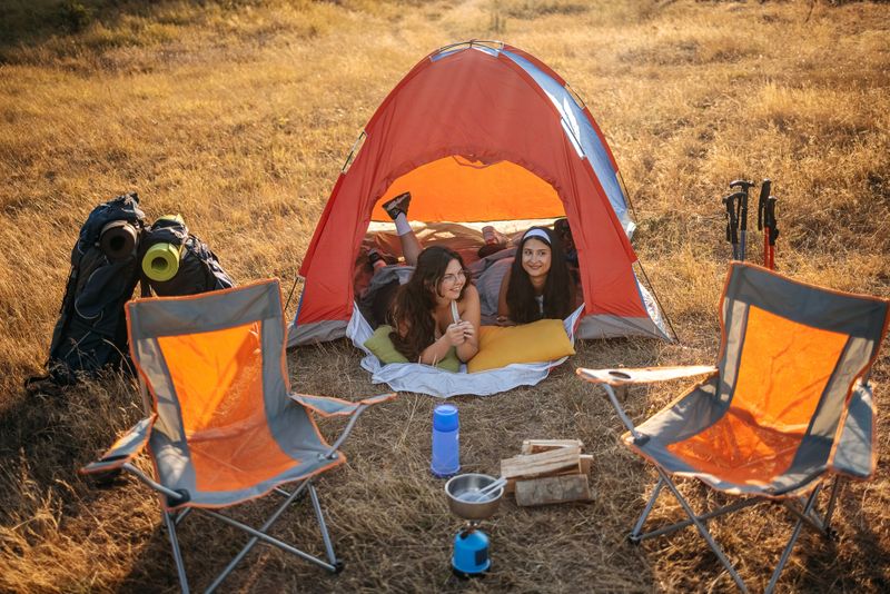 Close friends relaxing camping together in nature on sunny day and lying on front inside of tent while talking
