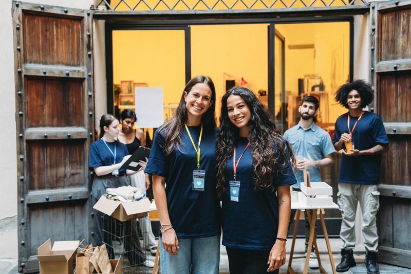Two young female volunteers smiling at the camera while working for a charity, organizing donations