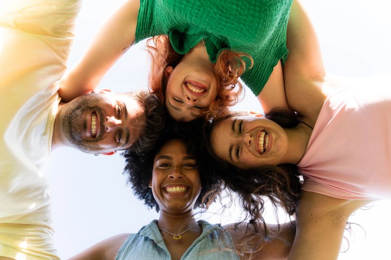Four young adult friends with heads together, forming a circle and smiling at the camera, low angle view