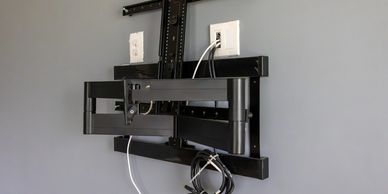 Wall-mounted TV bracket with cables attached to power outlets.