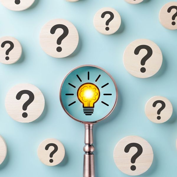 Magnifying glass highlighting a glowing light bulb among question marks.