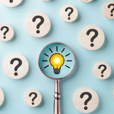 Magnifying glass highlighting a light bulb among question marks.