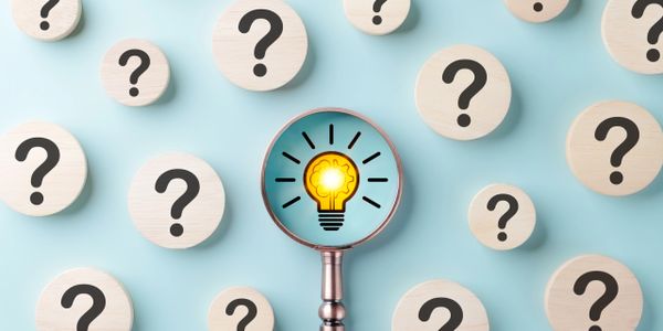 Magnifying glass highlights a glowing light bulb among question marks on wooden discs.