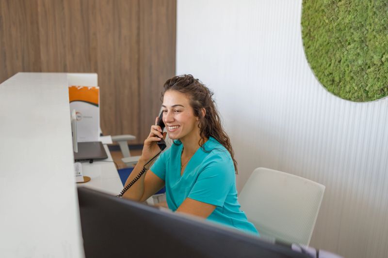 Young nurse smiling while answering phone calls at the reception desk of a modern medical clinic