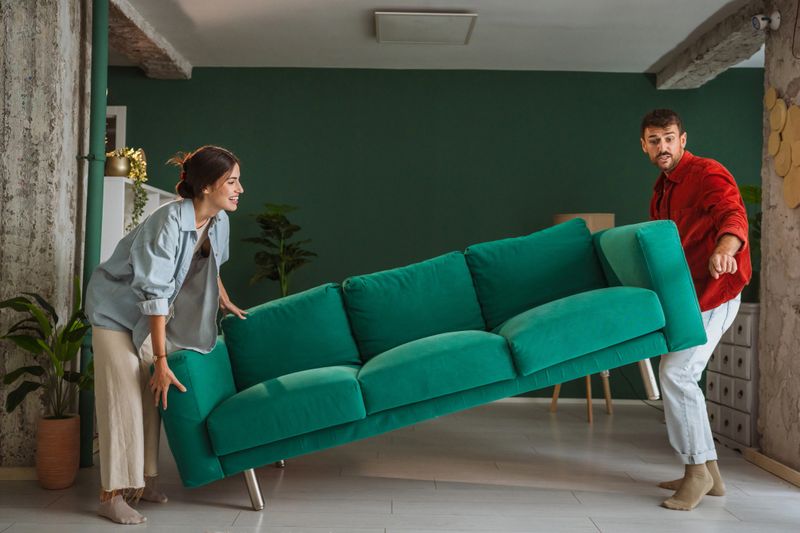 Young couple moving a vibrant green sofa in their modern apartment living room, rearranging furniture and crafting a cozy, inviting space for relaxation and togetherness
