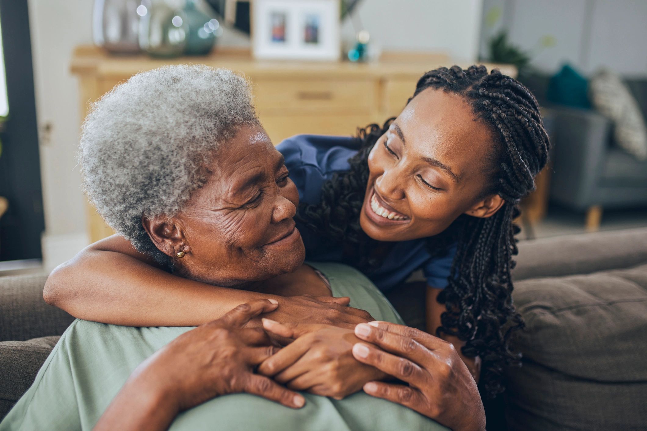 Young woman hugging elderly woman with joy.