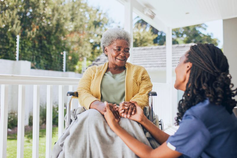 Young female nurse holding hands with an elderly patient in a wheelchair. Concept of assisted living at a nursing home.