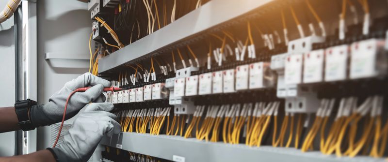 Electricity and electrical maintenance service, Engineer hand holding AC voltmeter checking electric current voltage at circuit breaker terminal and cable wiring main power distribution board.