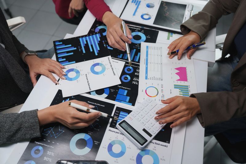 Business team analyzing financial charts and data at office desk, working together to achieve company goals