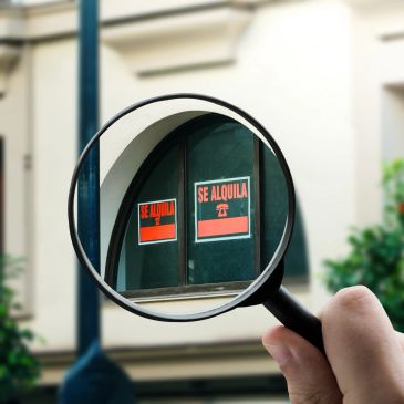 Magnifying glass showing 'Se Alquila' signs on a window.