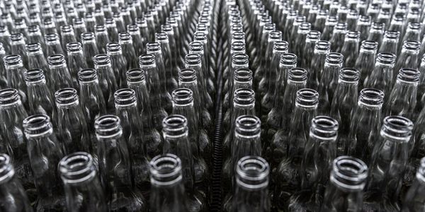 Rows of empty glass bottles lined up tightly in a factory or warehouse.
