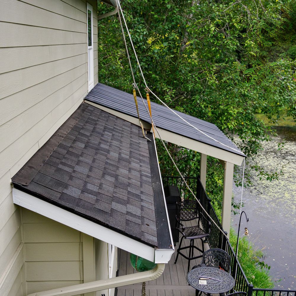 Riverfront porch with chairs, table, and fishing rods near lush greenery.