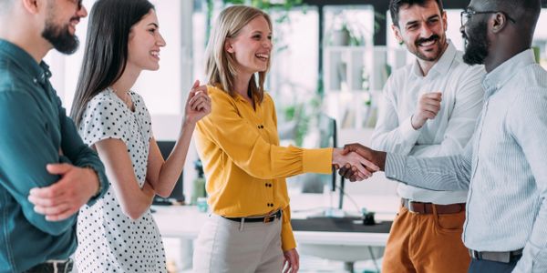 Colleagues smiling and shaking hands in a modern office setting.