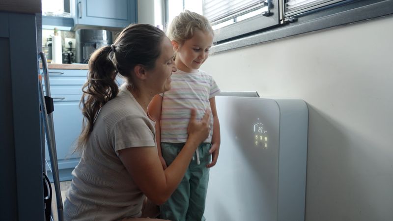 Family using energy at home. Mother teaching child how to use the smart control of home cooling & heating system. Ease of use of Artificial Intelligence in everyday life  Generic energy monitor in a kitchen setting.Needle on the Electricity dial jumps up into the red.