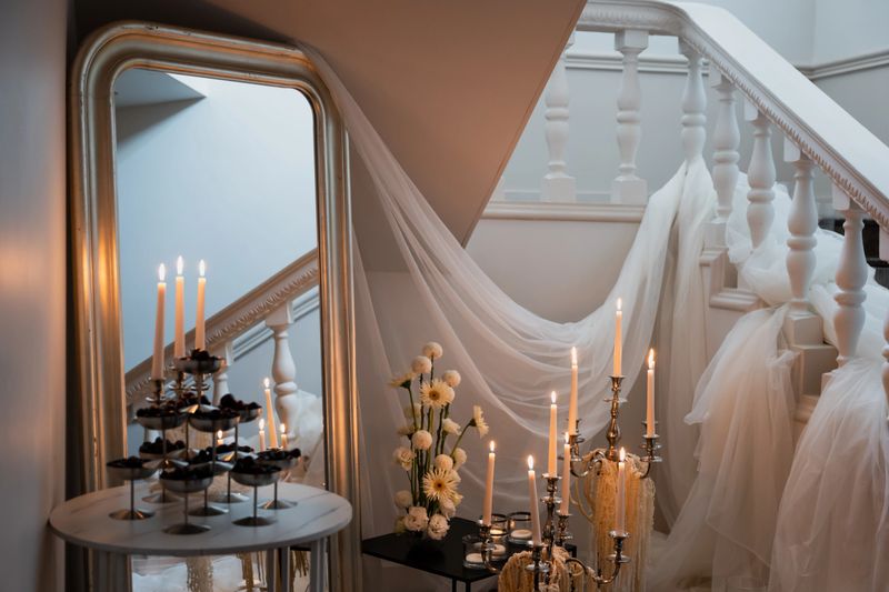 Beautiful wedding reception decor showcases candles, floral arrangements, and flowing fabric on a staircase, creating a romantic atmosphere