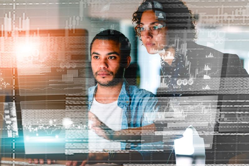 Two focused professionals working together, reviewing data and analytics displayed in a digital overlay to uncover meaningful insights and solutions.