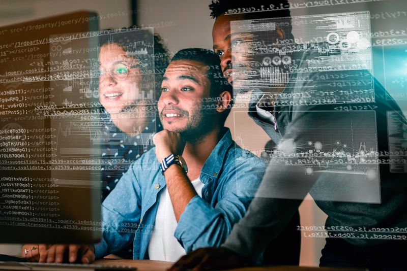 A group of professionals collaborates on a computer project, with digital overlays of code and visuals enhancing their work environment. Dynamic lighting and teamwork emphasize innovation and modern technology solutions.