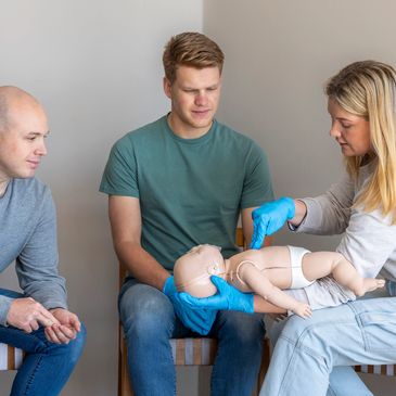 Three adults practicing infant CPR on a baby mannequin.