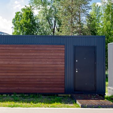 Modern black container building with wooden panel and black door.