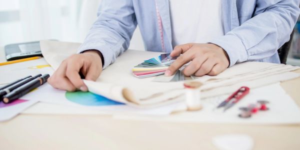Person selecting fabric color using a color swatch fan at a sewing workspace.