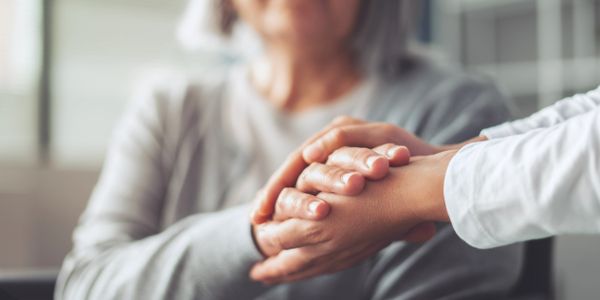 A person comforting an elderly woman by holding her hand.