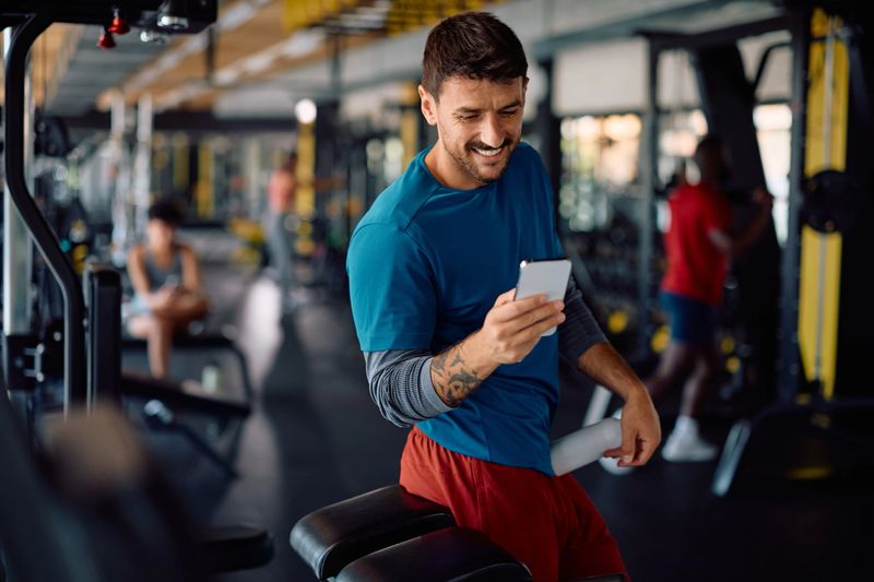 Happy athletic man using app on cell phone during gym workout. Copy space.