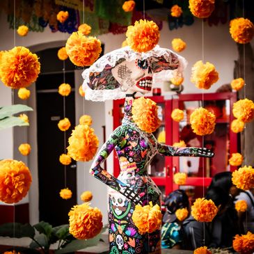 Decorated skeleton figurine surrounded by marigold flowers.