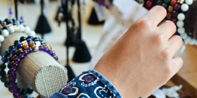 A hand wearing a bracelet among various colorful beaded bracelets on display.