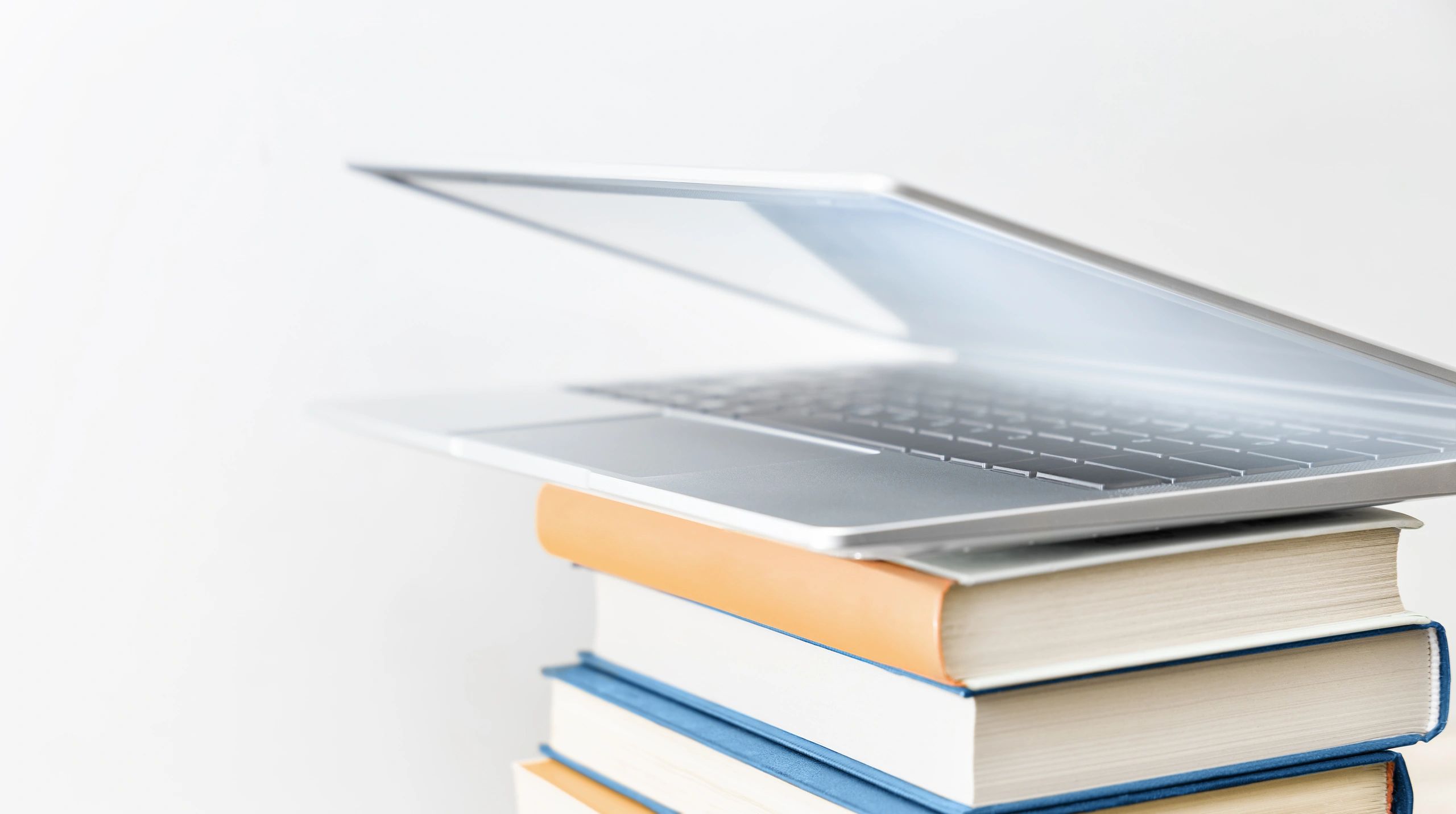 A laptop partially open on top of a stack of books.