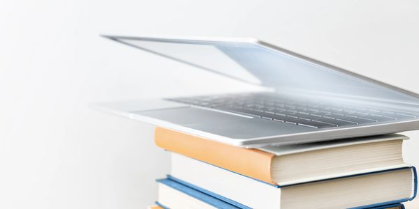 Laptop resting on a stack of books against a white background.