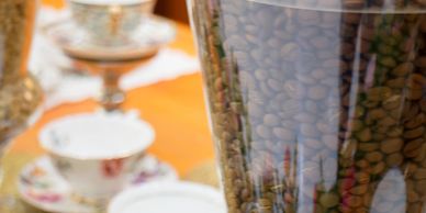 Close-up of coffee beans in a glass container with floral tea cups in the background.